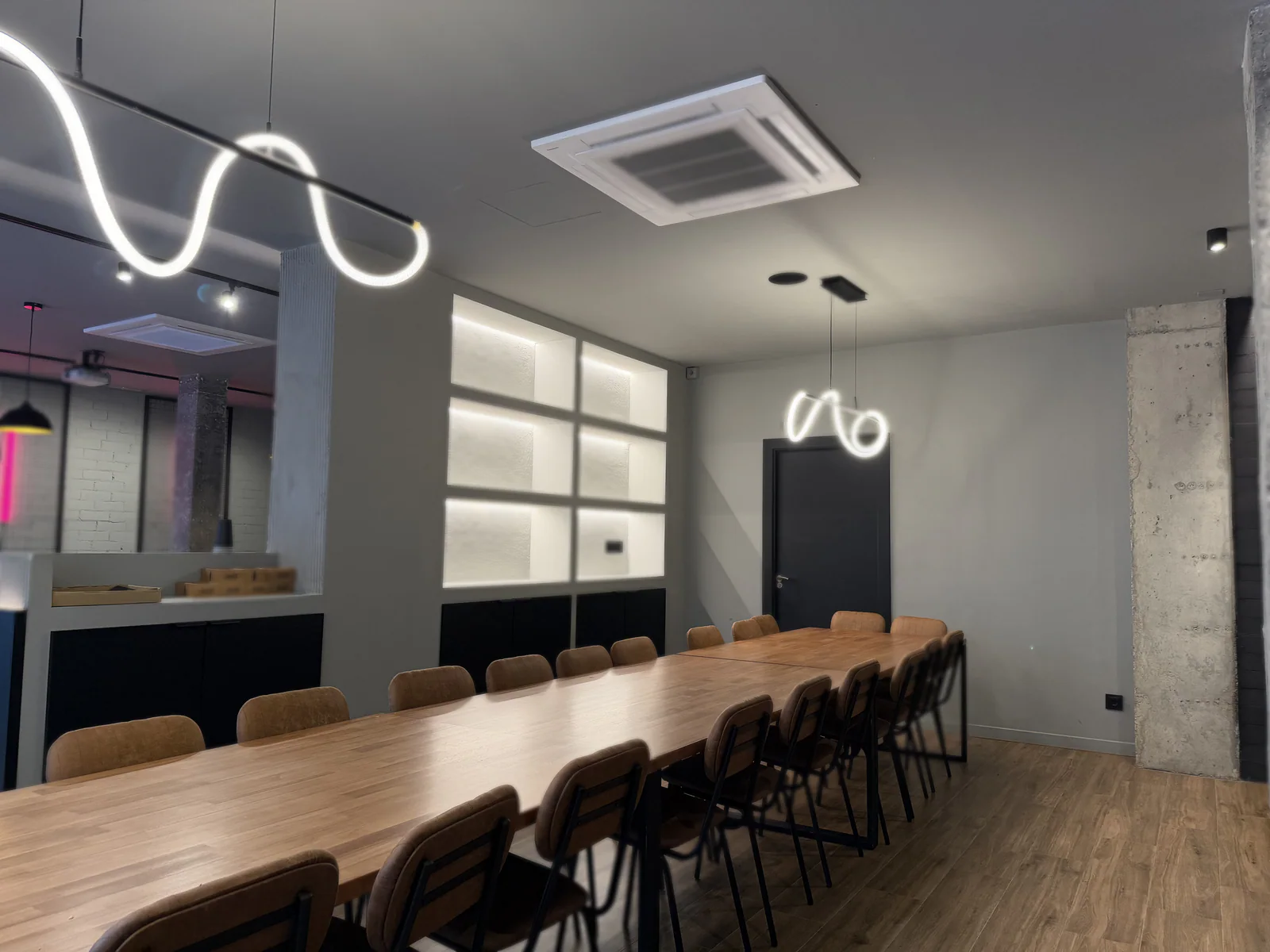 La mesa grande de abajo, larga y de madera, con sillas a los dos lados y las lámparas de luz ondulada