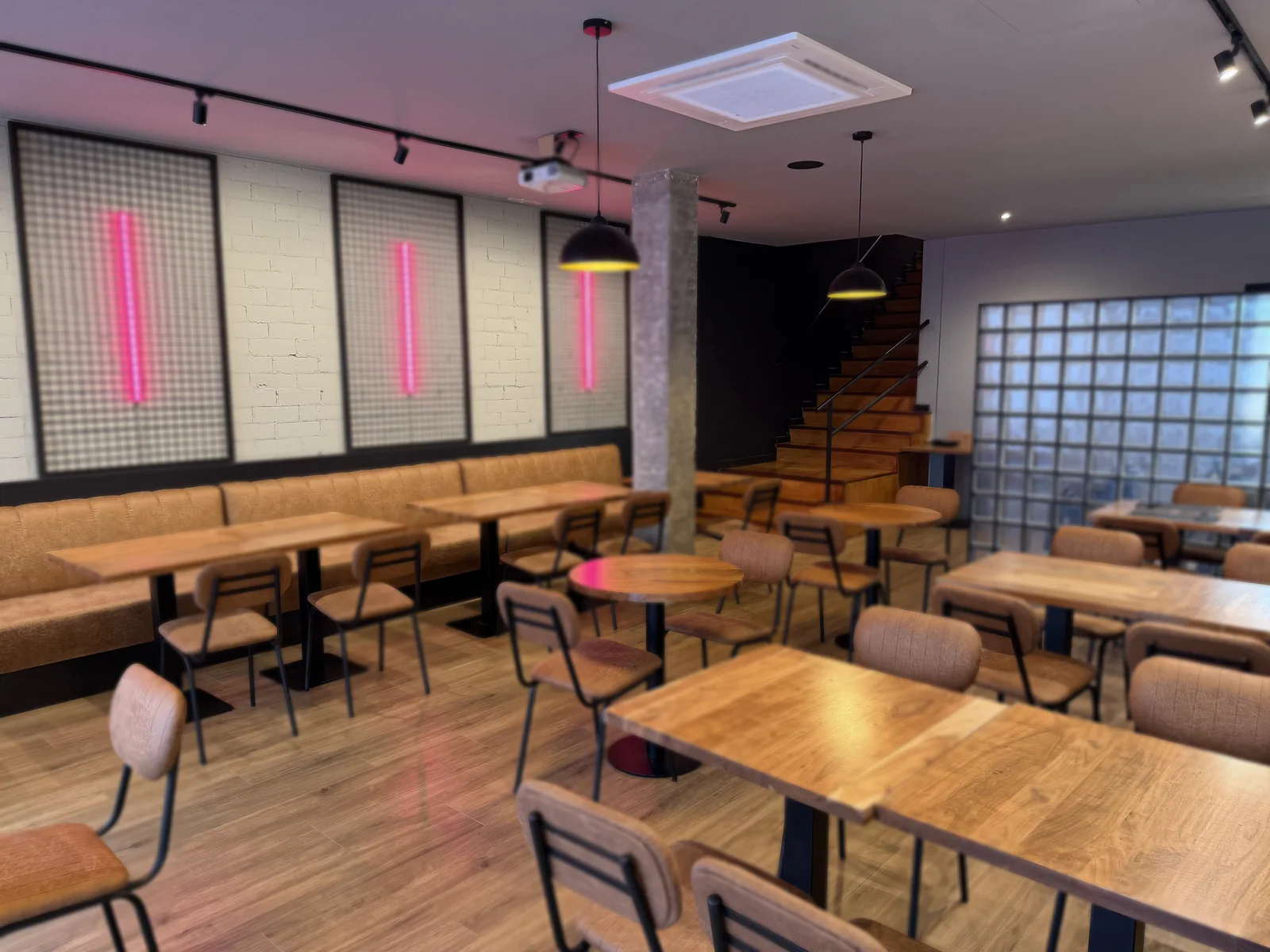 La sala de abajo: bancada de cuero, chapas negras con neones rosas y la escalera de madera al fondo