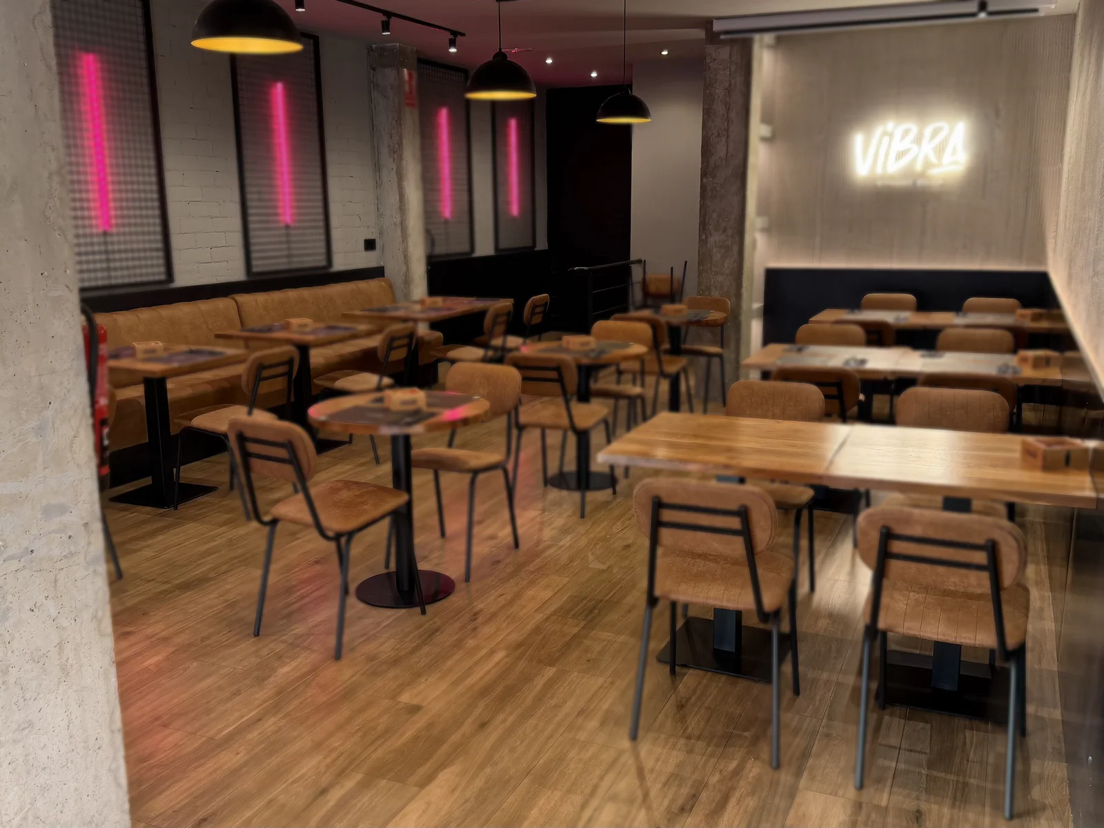 La sala de arriba: mesas de madera, sillas de cuero y el neón blanco con el nombre Vibra en la pared